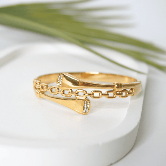 Gold bracelet with chain design on a white surface with green leaves in the background