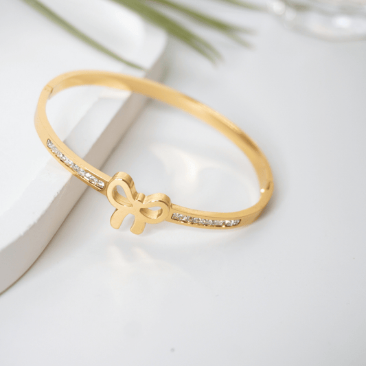 Gold bracelet with bow design on a light background