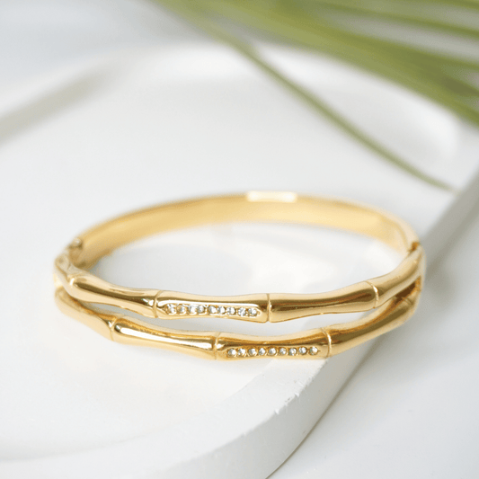 Gold bracelet on a white surface with a blurred green leaf in the background