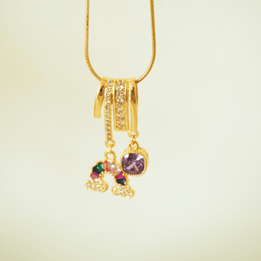 Gold necklace with a pendant featuring colorful gemstones on a light beige background