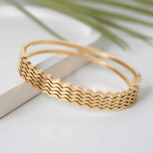 Gold bracelet with wavy pattern on a light background