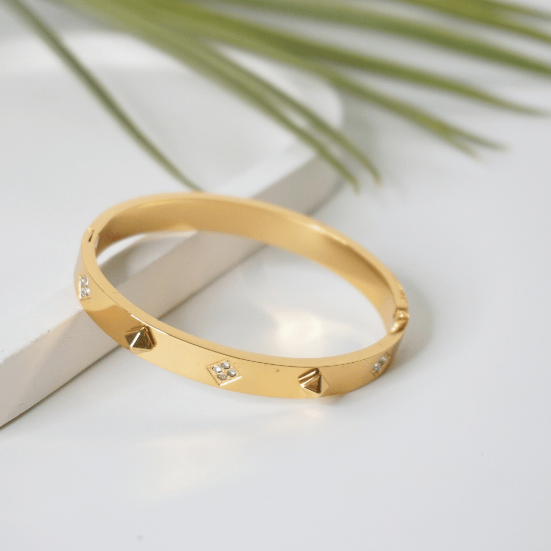 Gold bracelet with diamond accents on a light surface with a leafy background