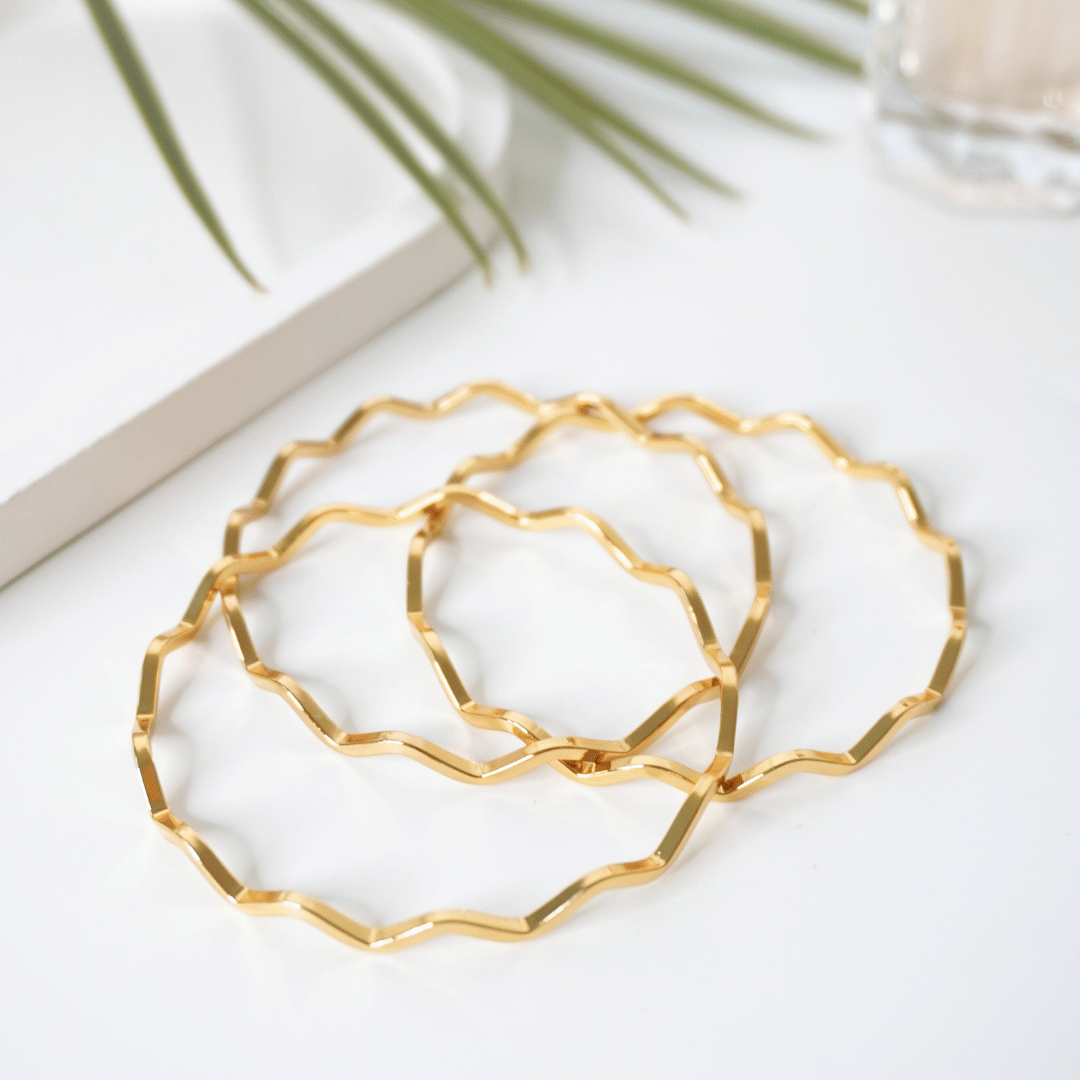 Gold geometric hoop earrings on a white surface with a plant in the background