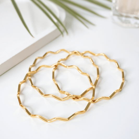 Gold geometric hoop earrings on a white surface with a plant in the background