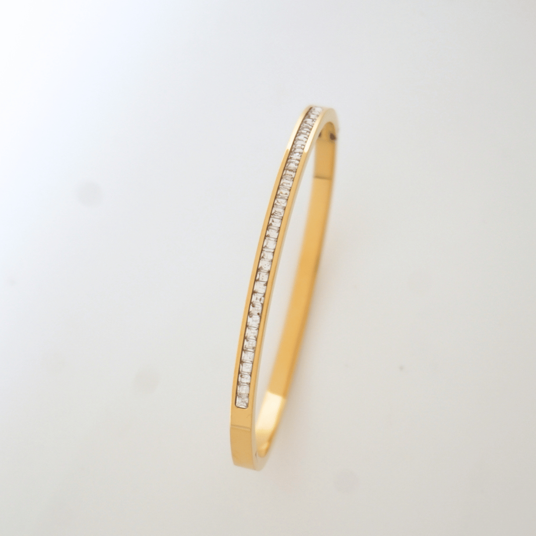 Gold bangle with embedded stones on a light gray background