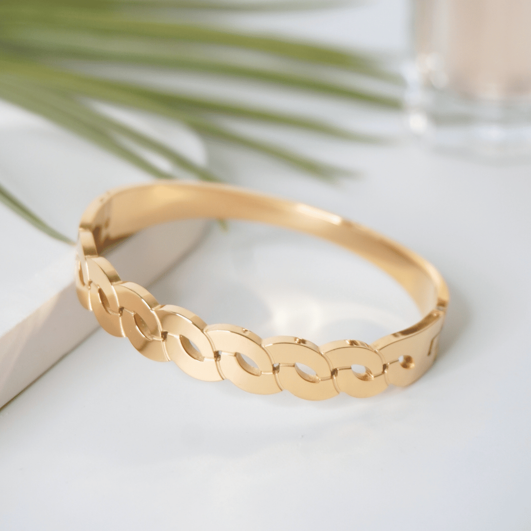 Gold bracelet on a light surface with green leaves in the background