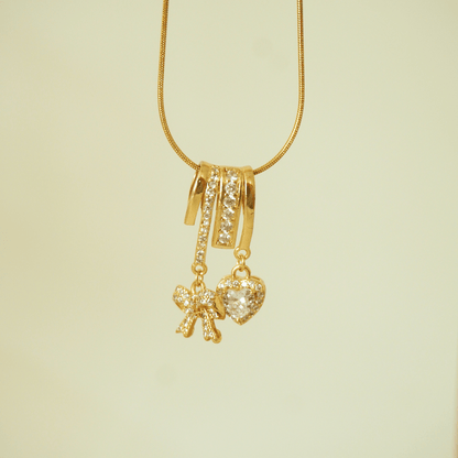 Gold necklace with heart and bow-shaped charms on a light green background