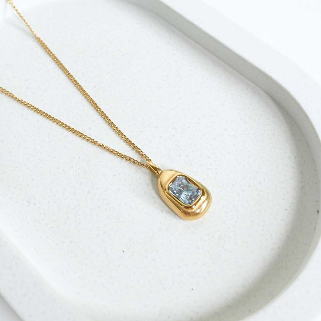 Gold necklace with a pendant featuring a blue gemstone on a white background