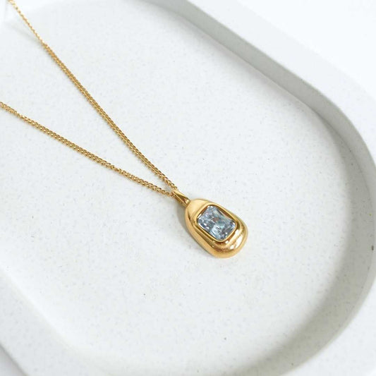 Gold necklace with a pendant featuring a blue gemstone on a white background