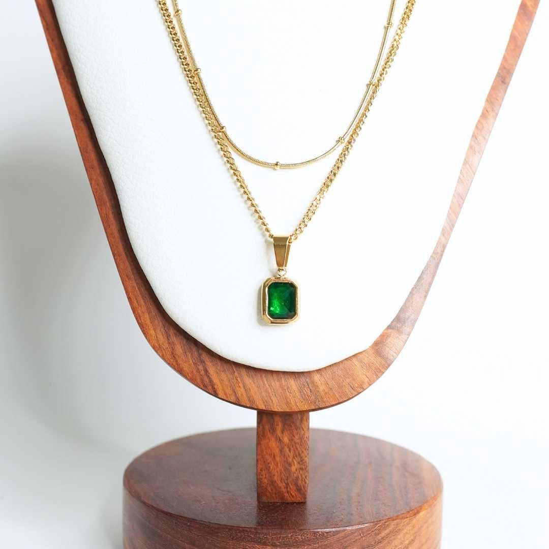 Gold necklace with a green pendant on a wooden stand