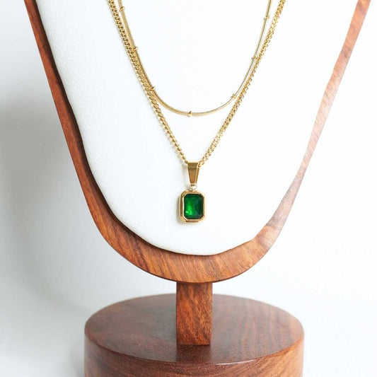 Gold necklace with a green pendant on a wooden stand