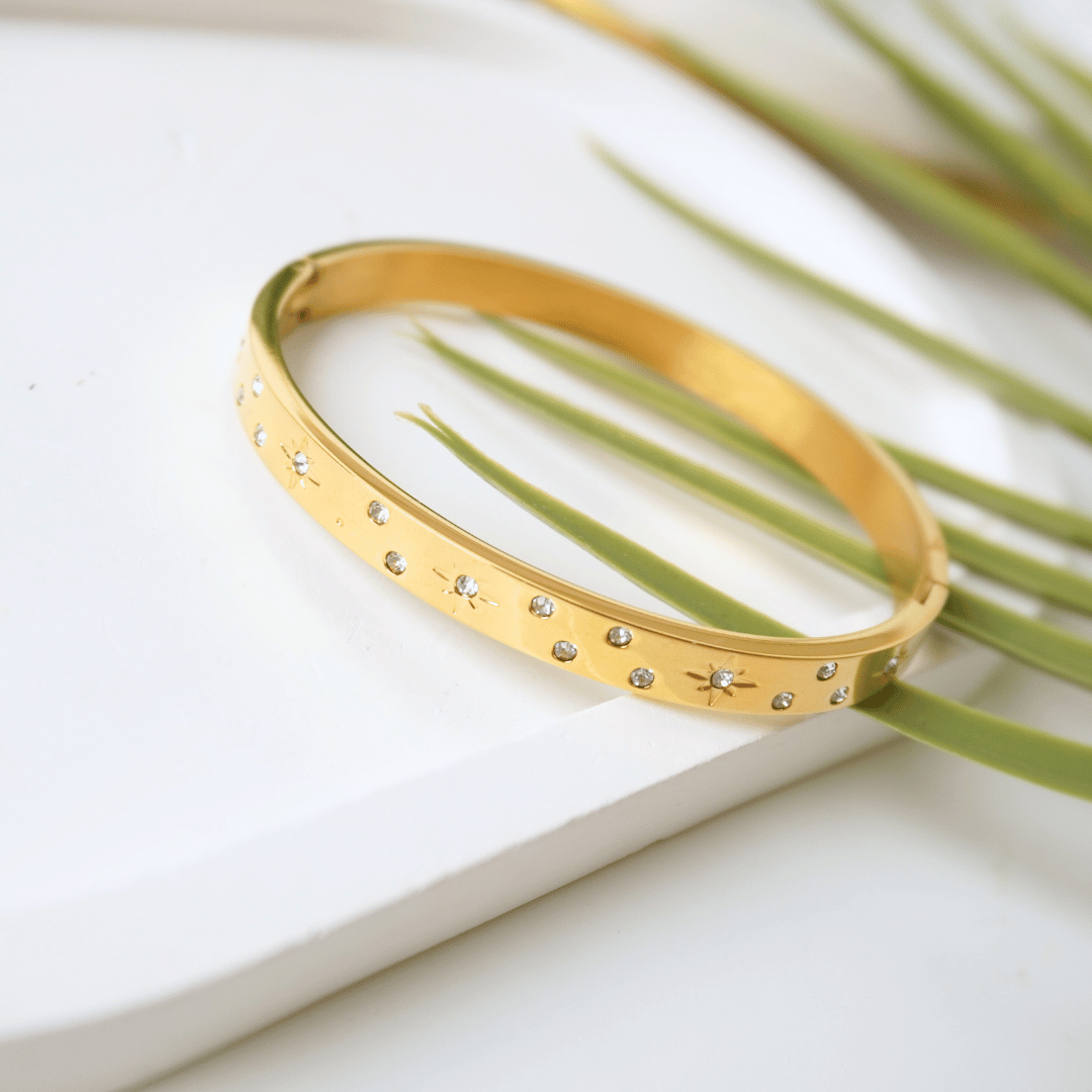Gold bracelet with small stones on a white surface with green leaves