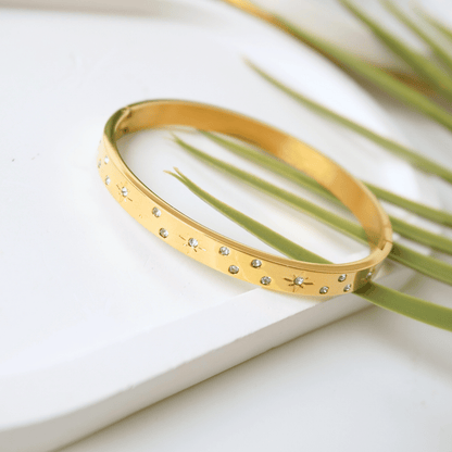 Gold bracelet with small stones on a white surface with green leaves