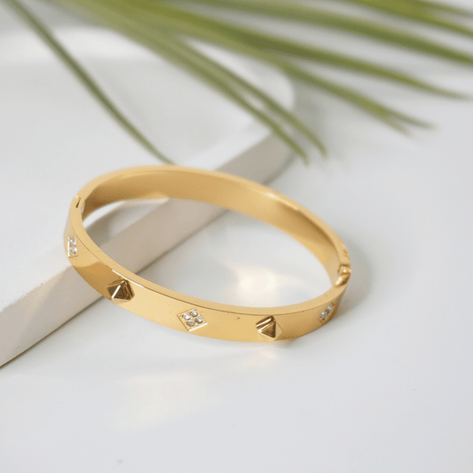 Gold bracelet with diamond accents on a light surface with a leafy background