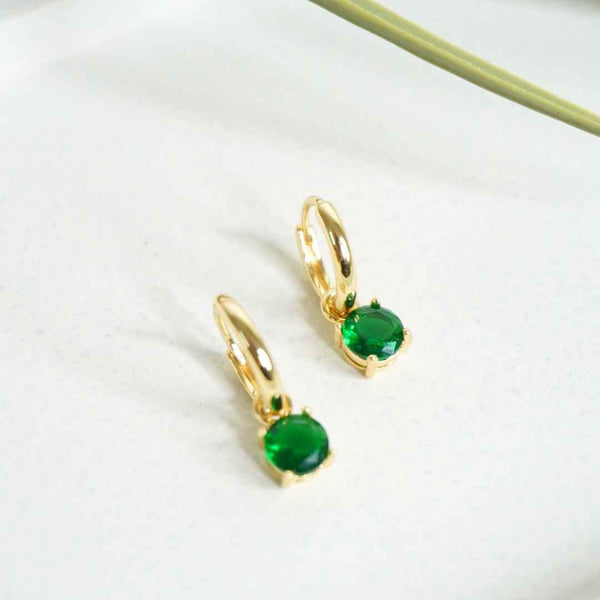 Gold hoop earrings with green gemstones on a white background
