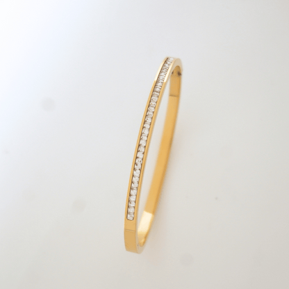 Gold bangle with embedded stones on a light gray background