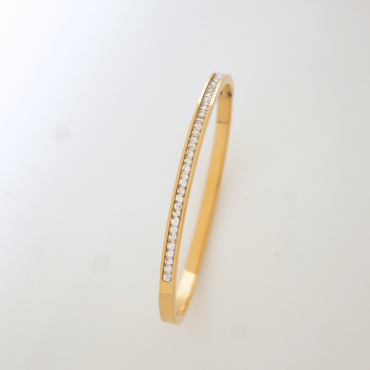 Gold bangle with embedded stones on a light gray background