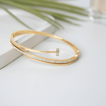 Gold bracelet with crystals on a light surface with green leaves in the background