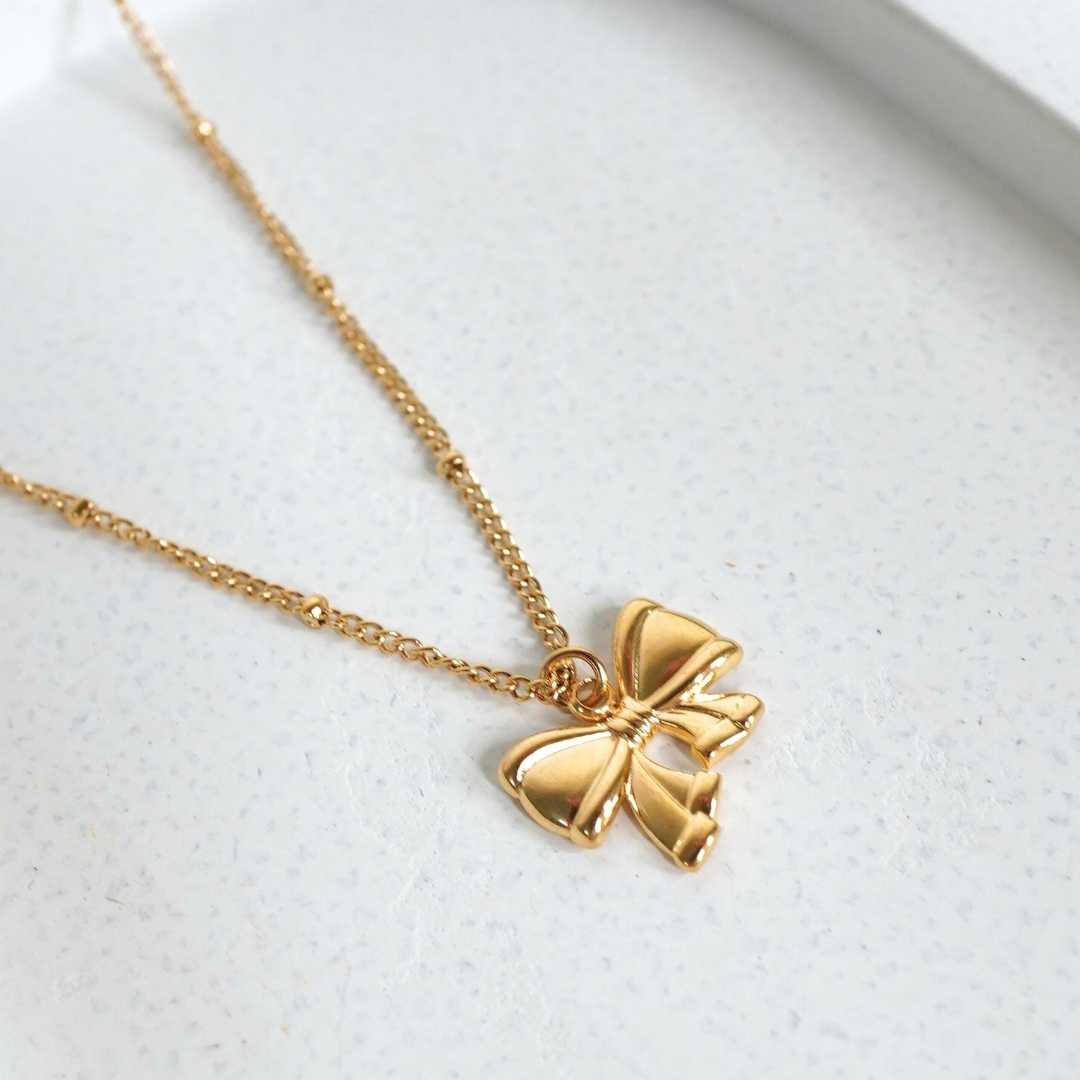 Gold bow-shaped pendant necklace on a light gray background