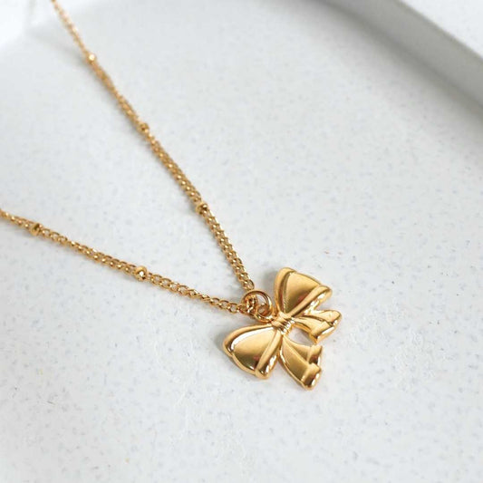 Gold bow-shaped pendant necklace on a light gray background