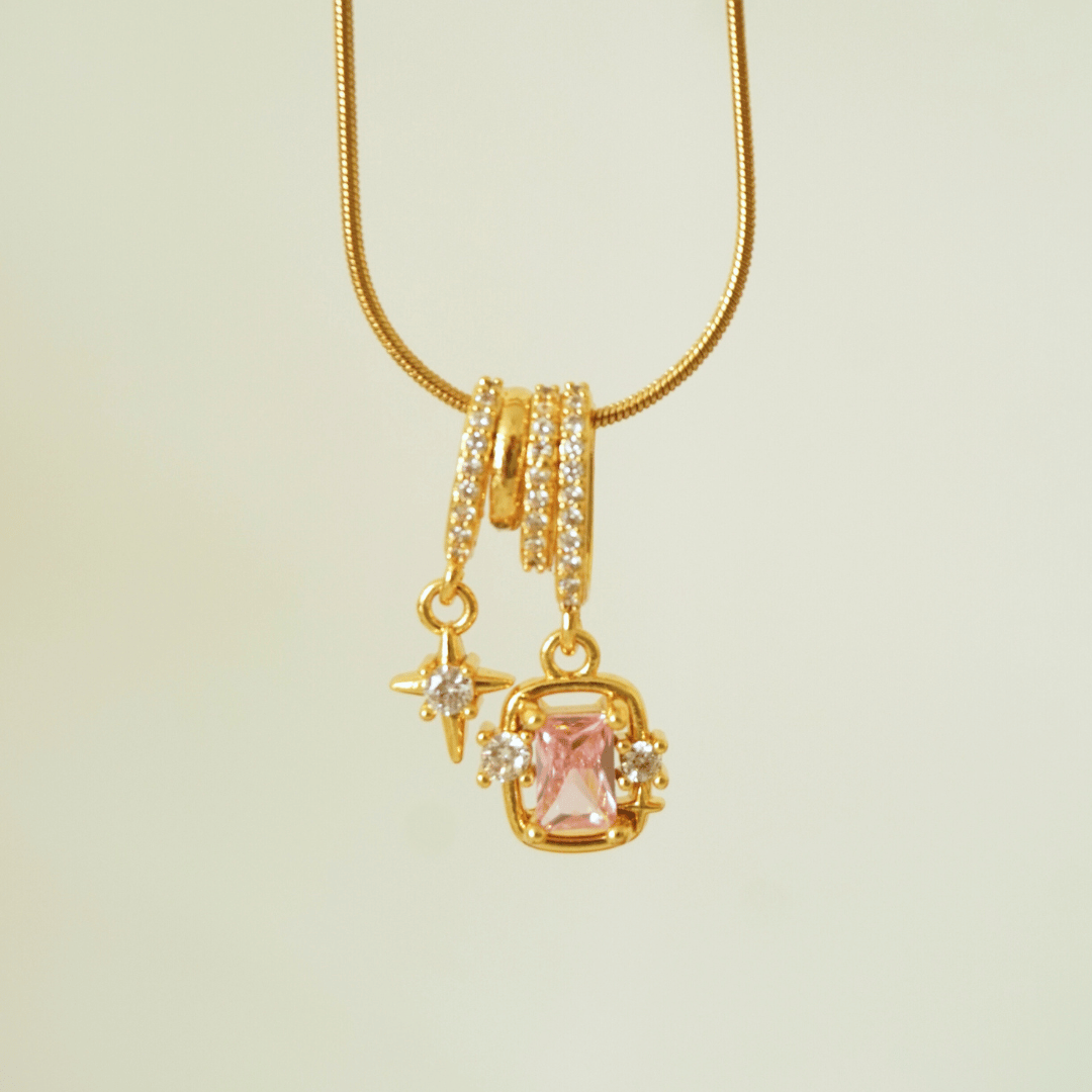 Gold necklace with a pink gemstone pendant on a beige background