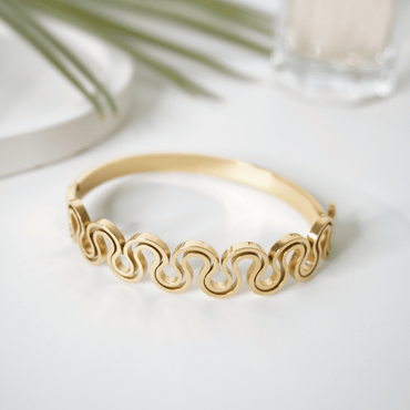 Gold bracelet with wave pattern on a light background