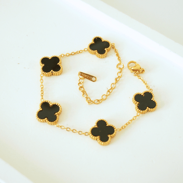 Gold bracelet with black clover-shaped charms on a white surface