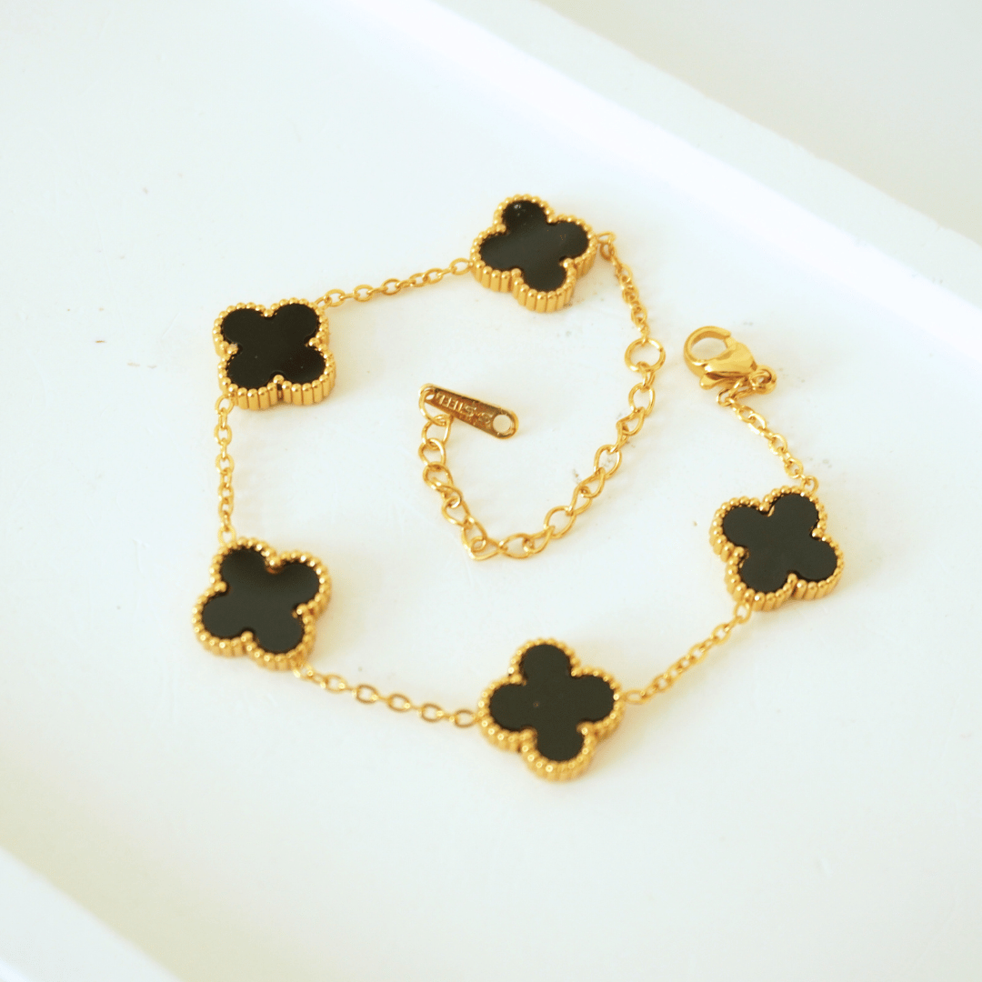 Gold bracelet with black clover-shaped charms on a white surface