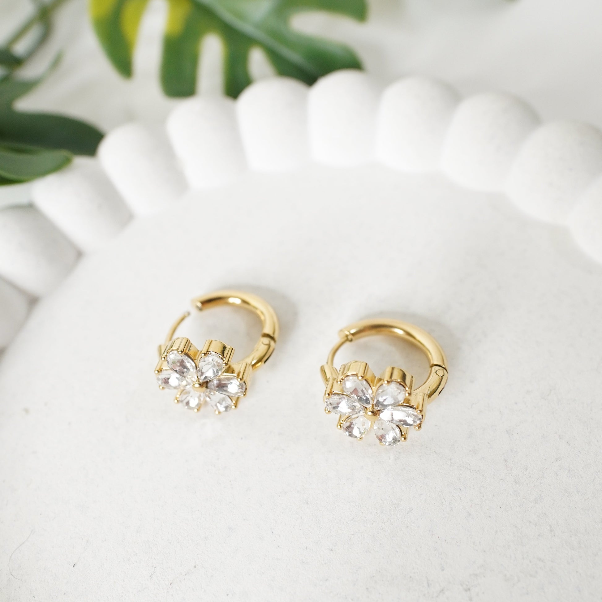 Gold hoop earrings with clear gemstones on a white surface with green leaves in the background, Anti tarnish earring, waterproof jewellery, Gold plated Jewelery, affordable Jewelery, anti tarnish jewellery, 